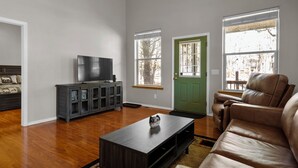 A living room with hardwood flooring, a dark wooden coffee table, a leather sofa, a television on a cabinet, and a green door.