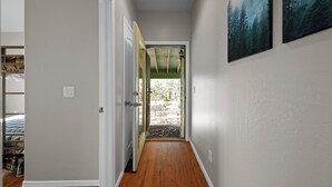 A hallway with wooden flooring, a white door, and a view of a forested area through an open door.