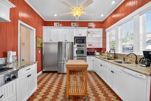 A kitchen with white cabinets, stainless steel appliances, a wooden bar stool, and a herringbone floor pattern. - Historic 1925 Estate · Pool · Sleeps 14 · 3.5 Baths · Walk to Marina (West Palm Beach)