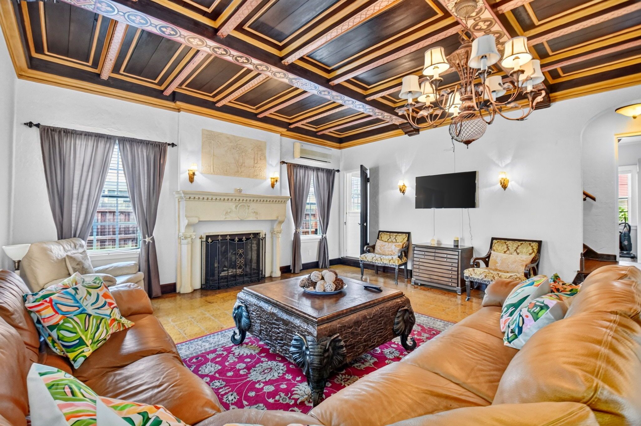 A spacious living room with a fireplace, leather sofas, a coffee table, and a chandelier.