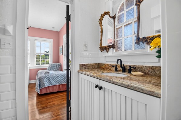 A bedroom with a bed, a bathroom with a sink and mirror, and a window with blinds.