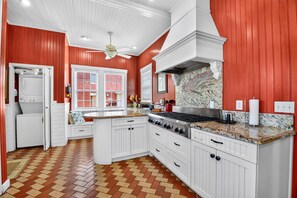 Una cocina con armarios blancos, una isla central, una estufa y una pared roja.