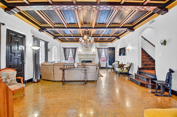 A spacious living room with a high ceiling, a fireplace, and a staircase.