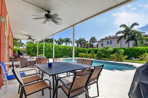 Un patio al aire libre con piscina, asientos cubiertos y ventilador de techo.