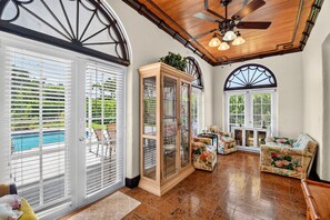A sunroom with large windows, a ceiling fan, and a wooden cabinet.