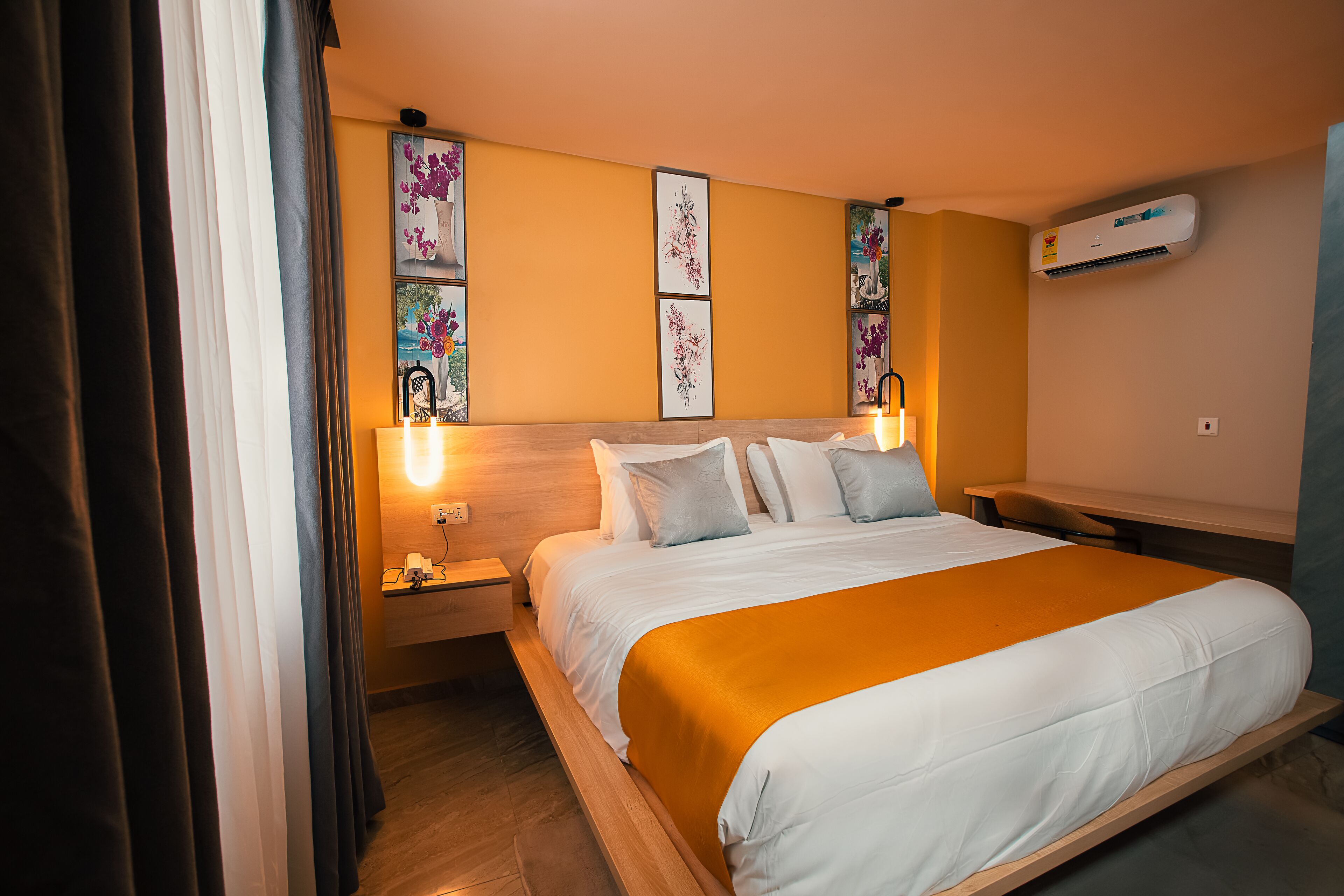 A hotel room with a bed, bedside tables, wall-mounted artwork, and an air conditioning unit.