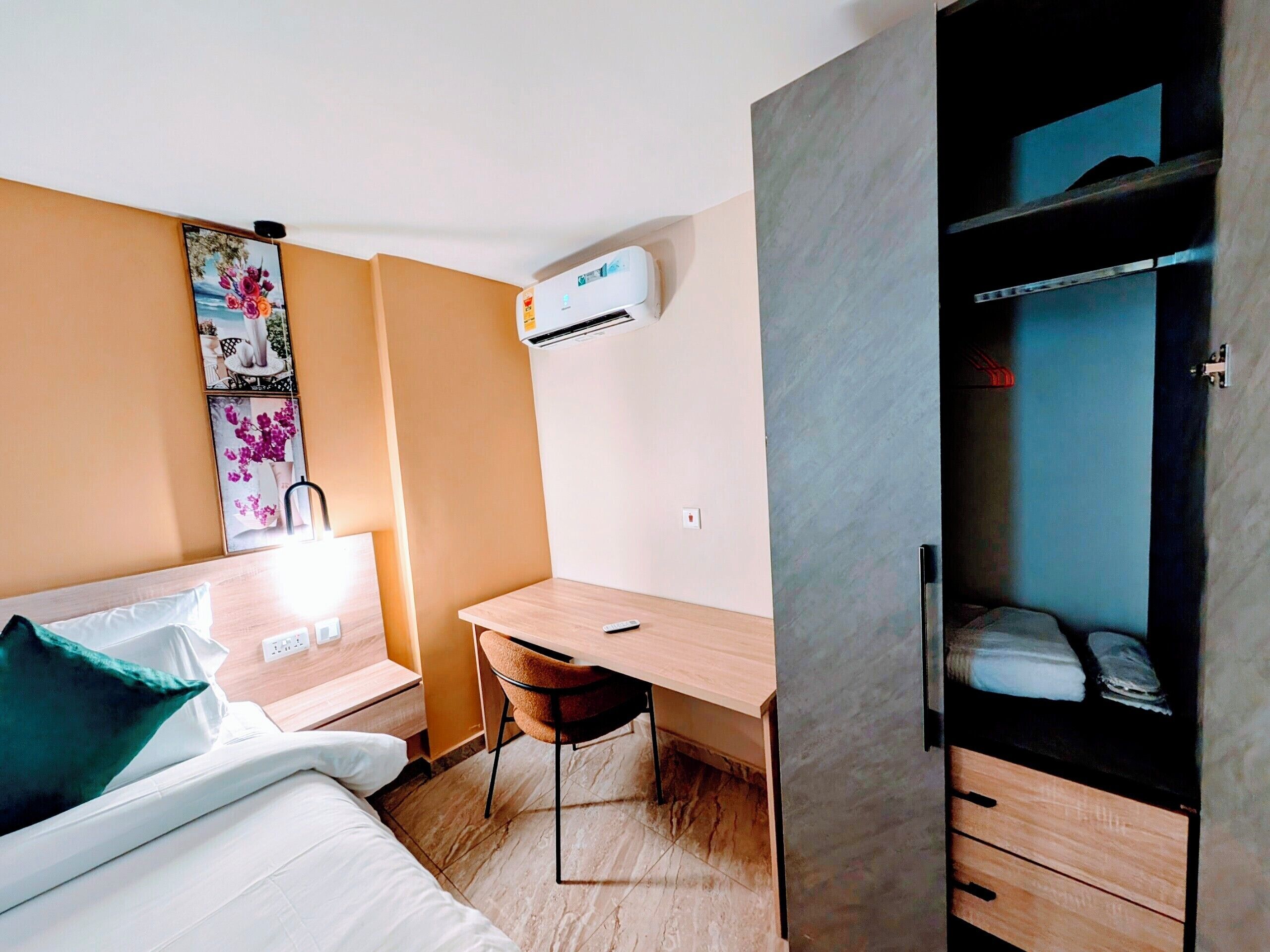 A hotel room with a bed, a desk, a chair, an air conditioning unit, and a wardrobe.