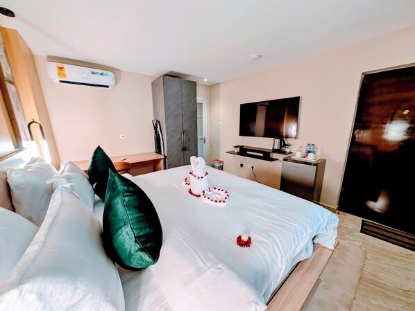 Et hotelværelse med seng, puder, et skrivebord, et fjernsyn og en aircondition.