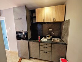 Una cocina compacta con armarios grises, un horno negro y un lavamanos de acero inoxidable.