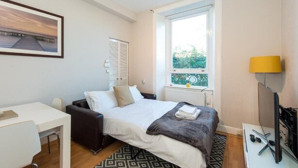 A bedroom with a bed, a desk, a chair, a window with a view, and a TV. - The Westfield, comfortable 2 bedroom apartment that sleeps 4 (Edinburgh)