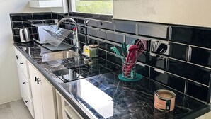 Una cocina compacta con encimera negra, armarios blancos y una ventana sobre el fregadero.