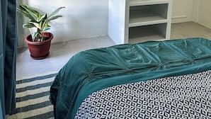 Un dormitorio con una cama, una planta en maceta, un televisor en la pared y un armario blanco.