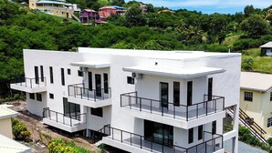 Un edificio moderno de varios pisos con balcones, rodeado de abundante vegetación y otros edificios residenciales.