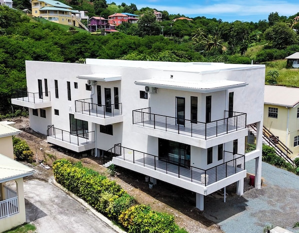 Un edificio moderno de varios pisos con balcones, rodeado de abundante vegetación y otros edificios residenciales.