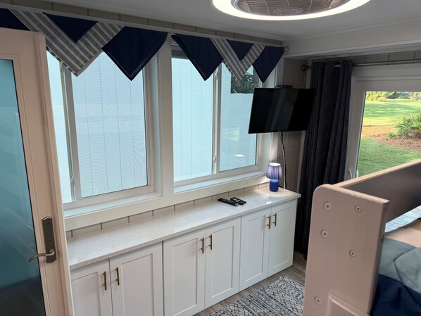 A bedroom with a window, a TV, a bedside table, and a bed.