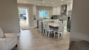 Une cuisine moderne avec des meubles blancs, un îlot central et un coin repas avec des chaises blanches.