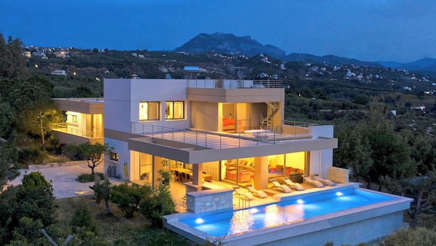 Ein modernes, zweistöckiges Haus mit Swimmingpool, Außenbereich zum Sitzen und Blick auf die umliegende Landschaft.
