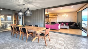 Ein moderner Essbereich mit Holztisch und -stühlen, im Hintergrund eine Küche und ein Wohnzimmer mit rosa Sofa und einer Chandelier.