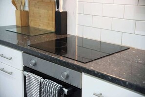 Uma cozinha com fogão por indução preto, armários brancos e painel de azulejos.