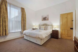 A bedroom with a bed, bedside tables, a wooden door, and a window with curtains. - 5BR in Queen Street with WiFi, Backyard, Parking (Redcar and Cleveland)