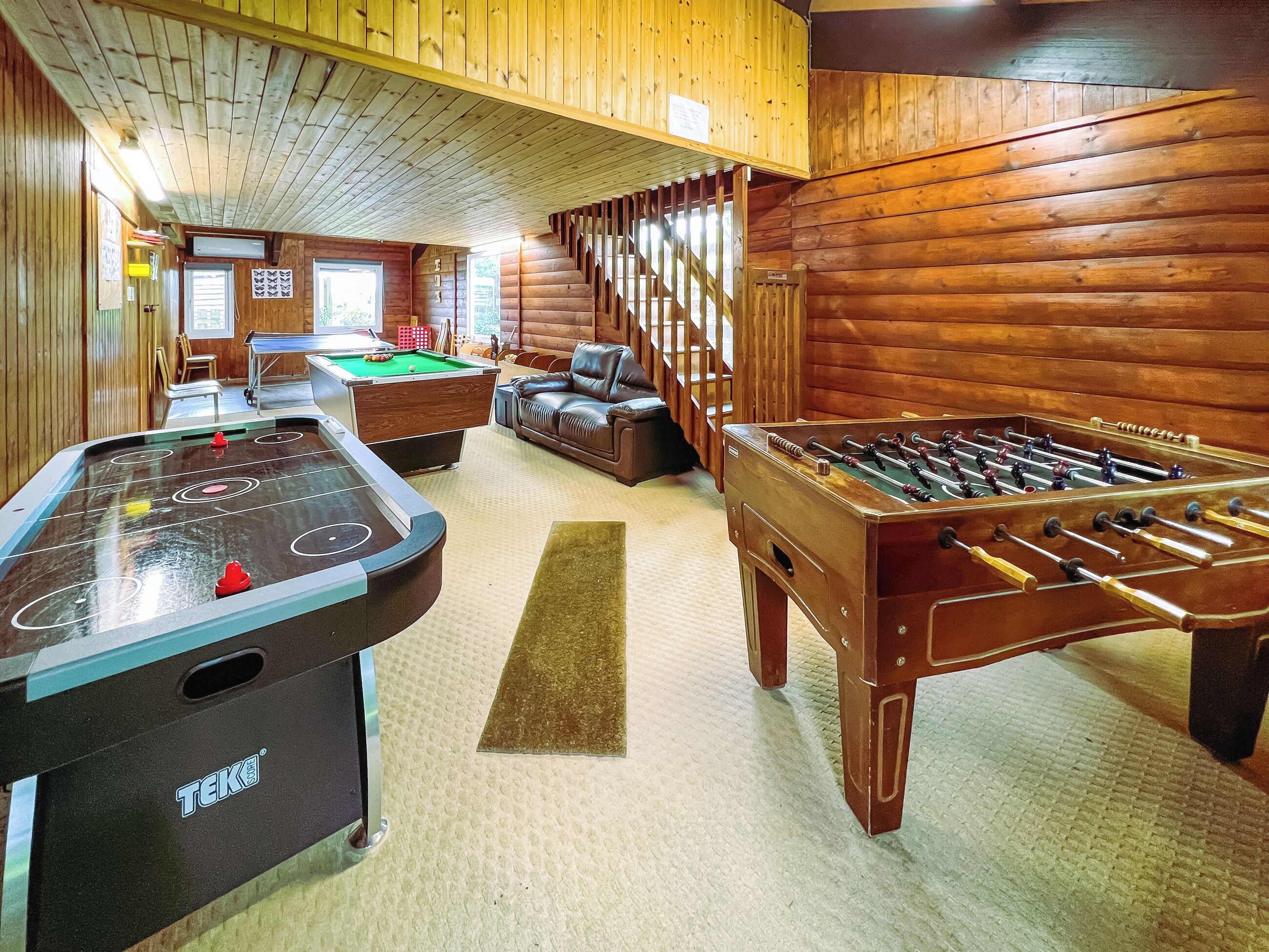 Ein Raum mit Holzboden, einer Tischfußballplatte, einem Billardtisch und einem Snookertisch.