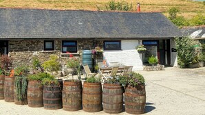 A stone building with a sloped roof, multiple windows, and a gravel driveway. - Linney Cottage - UK48986 (Looe)