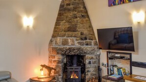 A cozy living room with a stone fireplace, a comfortable sofa, a television, and a small table with books. - Linney Cottage - UK48986 (Looe)
