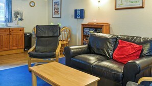 Ein Wohnzimmer mit Ledersofa, einem Holztisch, einem Essbereich mit einem Holzhocker, einer Küche mit Holzschränken und einer an der Wand hängenden Karte.
