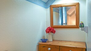 Ein Badezimmer mit einem Holzkosmetikschrank, einem Spiegel und einer Vase mit roten Blumen.