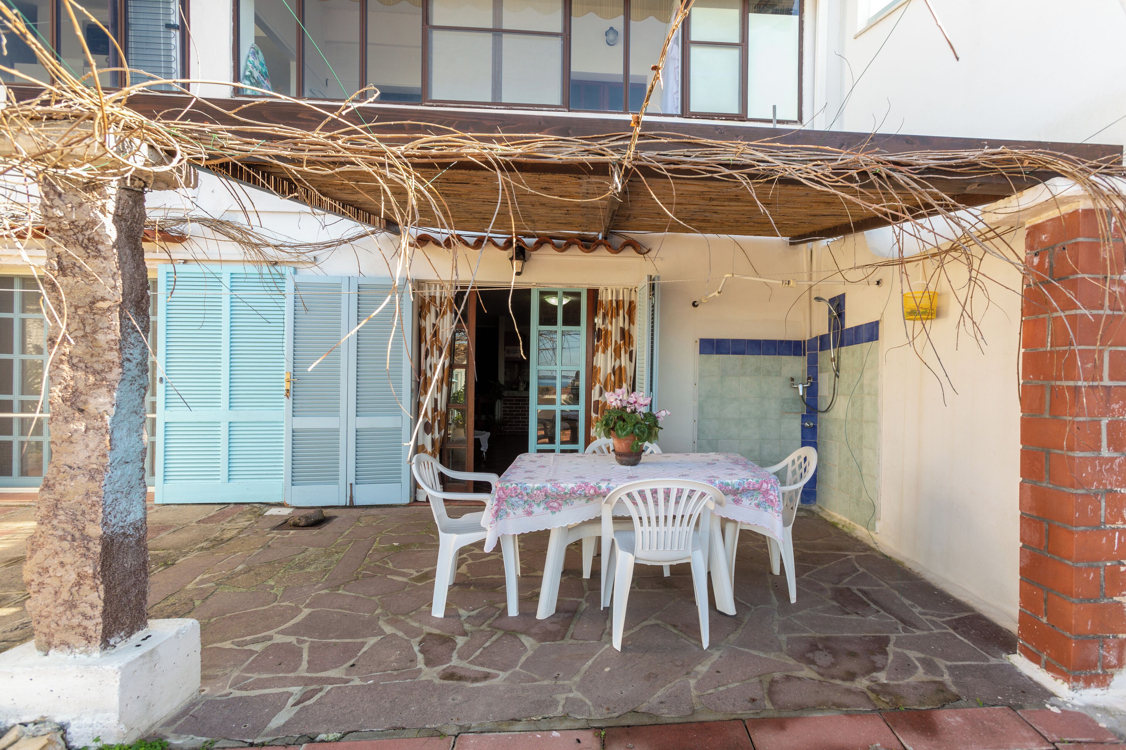 A patio with a table and chairs, a potted plant, and a building with blue shutters in the background.