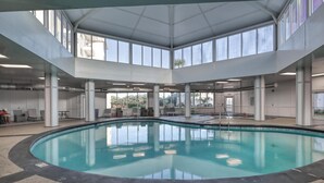 A large indoor swimming pool with a clear view of the sky through large windows, surrounded by a tiled floor and white pillars. - New owner Beautiful Beach view,Indoor pool & Hot Tub (Gulf Shores)