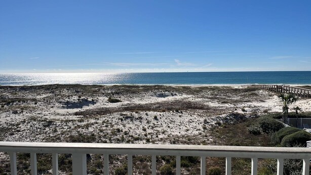 A beach view with a wooden boardwalk leading to the ocean, sandy dunes, and sparse vegetation. - New owner Beautiful Beach view,Indoor pool & Hot Tub (Gulf Shores)