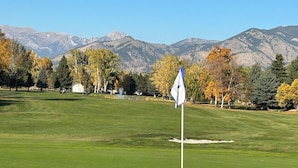 A golf course with a flagstick, a pond, and mountains in the background. -  Great Montana Townhouse Skiing, Fly Fishing, Golf all in your backyard! (Bozeman)