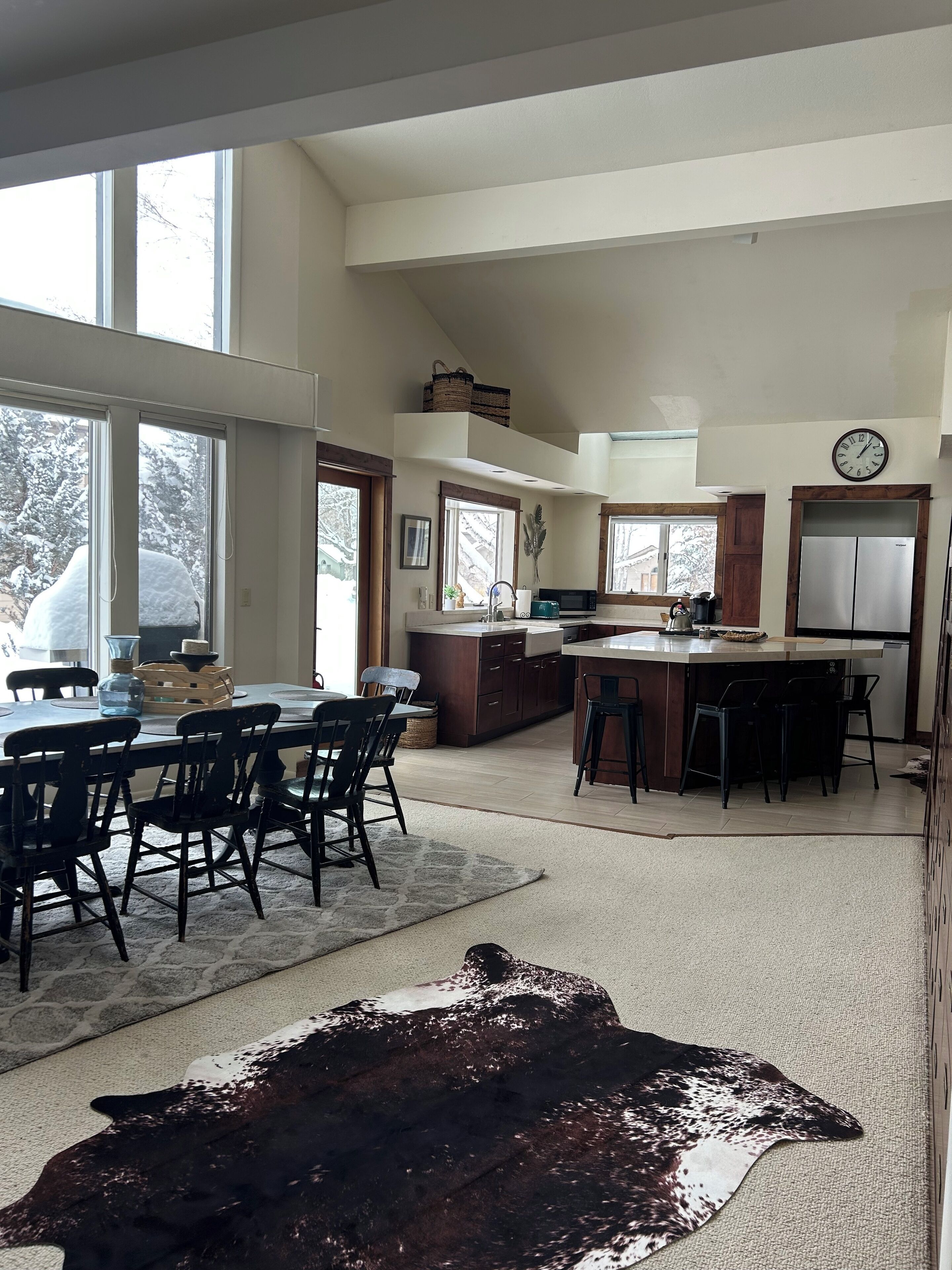 A spacious kitchen with a dining area, large windows, and a unique leather rug.