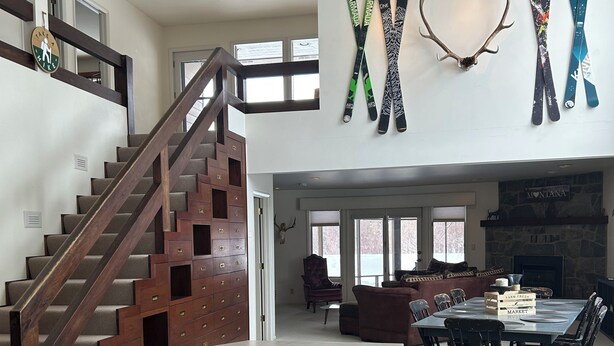 A spacious kitchen with a central island, a dining area with a large table and chairs, a staircase with wooden railings, and a fireplace with a stone mantle. -  Great Montana Townhouse Skiing, Fly Fishing, Golf all in your backyard! (Bozeman)