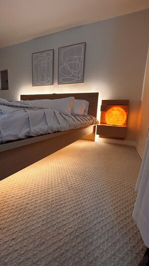 Un dormitorio con cama, una mesita de noche con lámpara y arte abstracto en la pared.