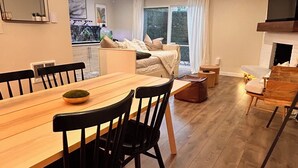 Amplia sala de estar con una mesa de comedor de madera, sillas negras, un sofá y un televisor.