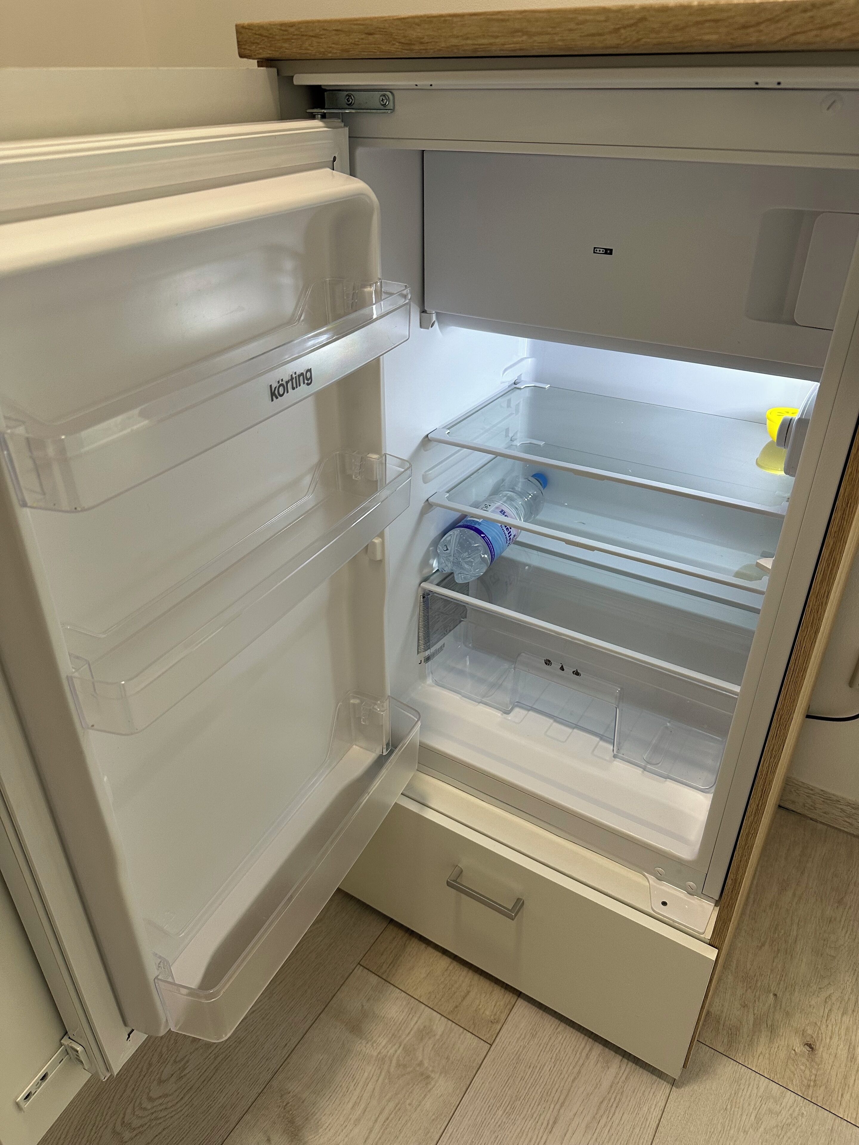 Un réfrigérateur ouvert, avec des étagères en plastique transparent et une bouteille d’eau sur l’étagère supérieure.