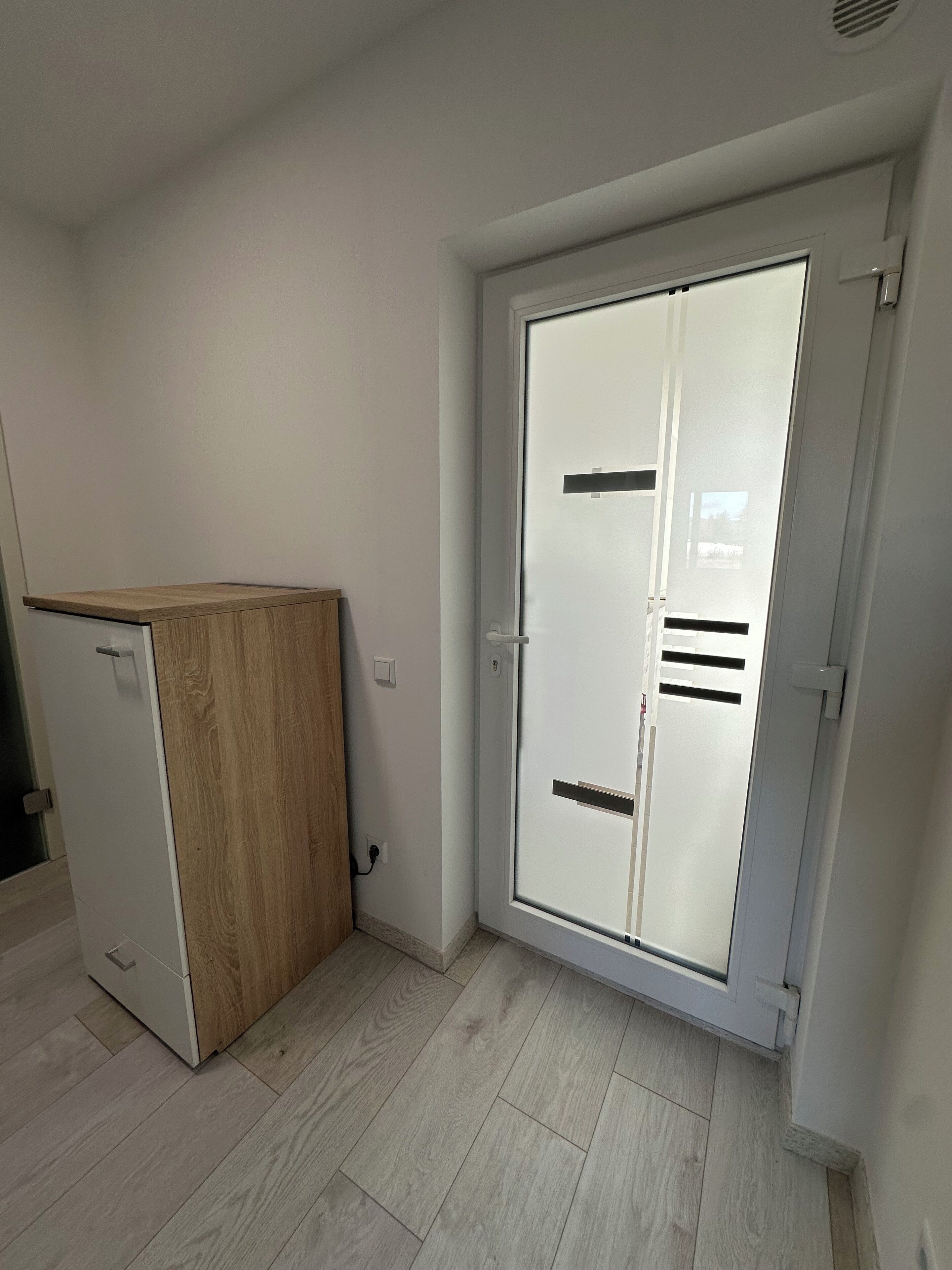 Une pièce dotée d’une porte coulissante, d’un petit meuble en bois et d’un plancher de couleur claire.