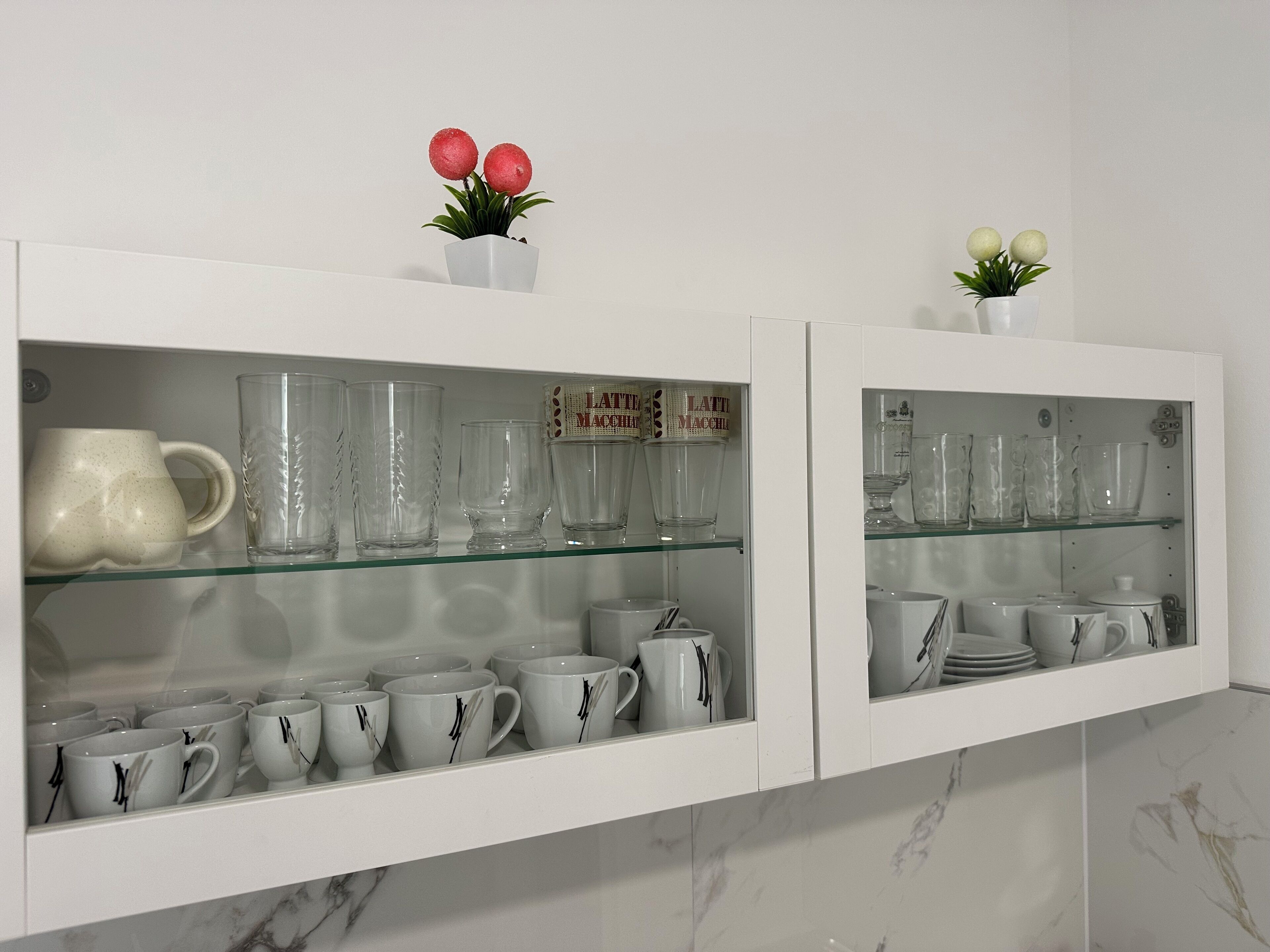 Dos vitrinas blancas con estantes de vidrio, cada una con diferentes vasos y tazas de cerámica.