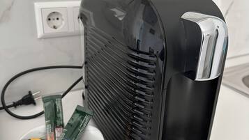 A black portable heater with a power cord plugged into a wall socket.