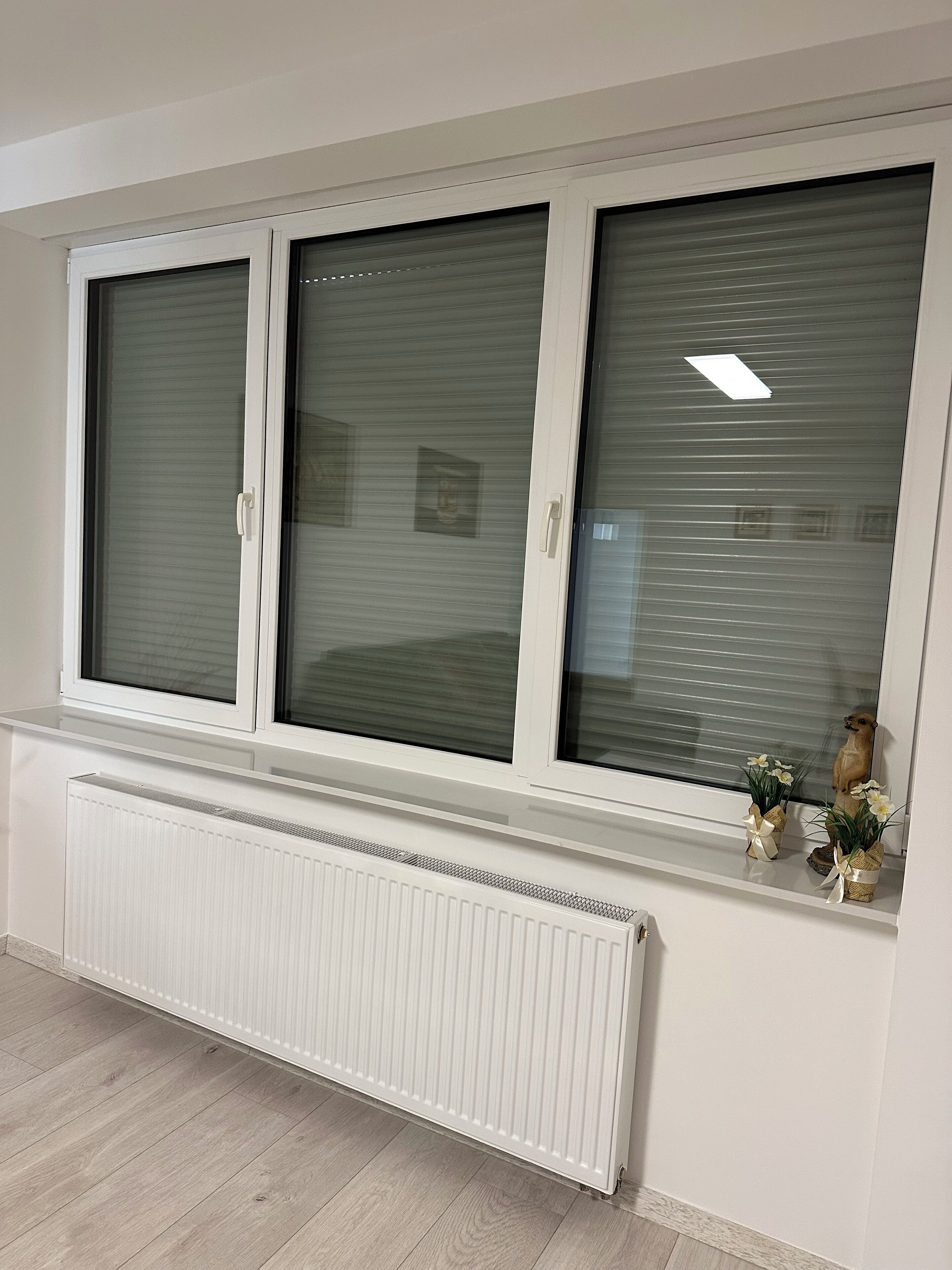Ein Zimmer mit weißem Heizkörper, einem Fenster mit Jalousien und einem kleinen Regal mit Dekoration.