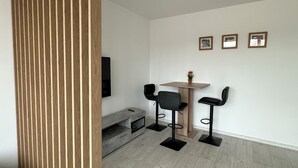 A modern room with a wooden partition, a dining table with two chairs, a TV mounted on the wall, and three framed pictures. - Comfort vacation apartment NeuBau Merzig (Merzig)