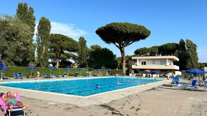A swimming pool with lounge chairs and umbrellas, surrounded by trees and a building. - Spacious Villa with Pool, BBQ and Tennis Courts (Lazio)