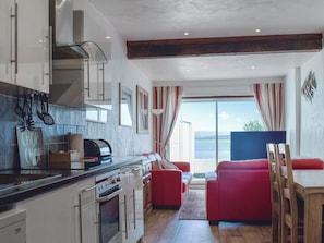 Une cuisine équipée d’une cuisinière, de placards et d’un coin repas avec un canapé et une table rouges.
