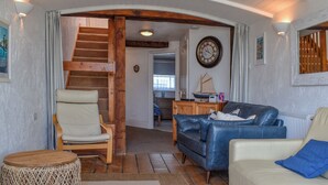 Ein Wohnzimmer mit Treppe, einer Uhr, einem Sofa, einem Sessel und einem runden Holztisch.