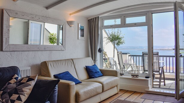 Ein Wohnzimmer mit Sofa, Sessel, Tisch, einem Balkon mit Meerblick und einem großen Fenster.