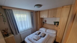 Ein Schlafzimmer mit einem Bett, Holz-Kopfteil, einem Fenster mit Vorhängen, einer Heizung und einem Regal mit Dekoration.