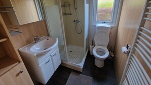 Ein kleines Badezimmer mit Dusche, Toilette, Waschbecken und Fenster.