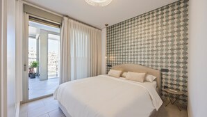 A bedroom with a large bed, a view through a sliding door to an outdoor balcony, and a patterned wall.